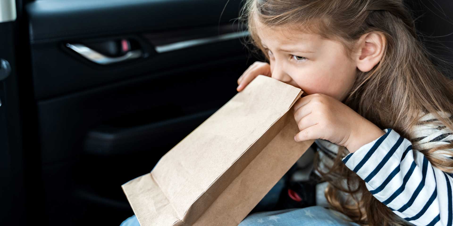 Ein Mädchen sitzt im Auto und hält einen braunen Papiertüte nah an den Mund.