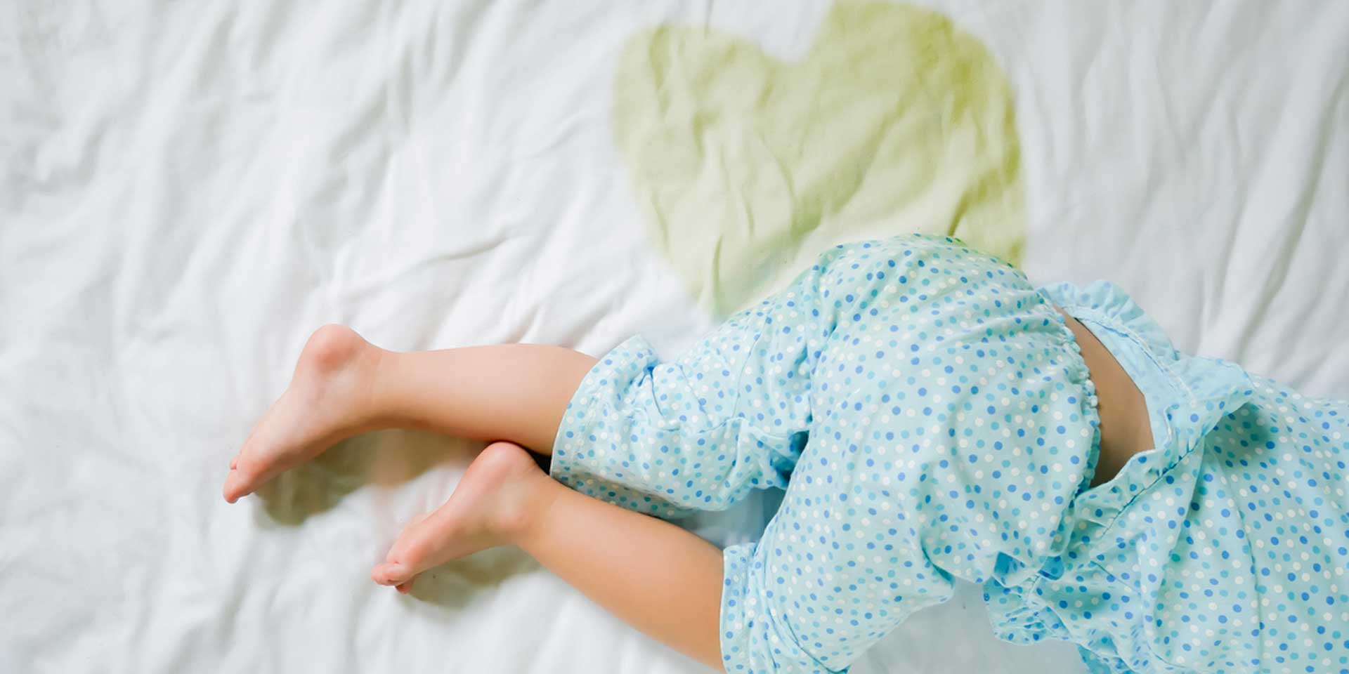 Ein Kind liegt auf einem Bett, umgeben von einer nassen Stelle auf der Decke.