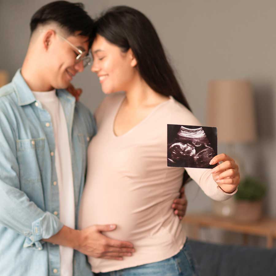 Glückliches Paar freut sich auf ein Baby, hält Ultraschallbild in die Kamera.